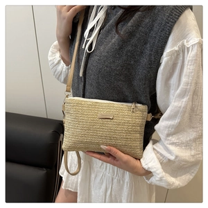Detail of beige woven straw crossbody bag with chevron pattern and gold metal plate