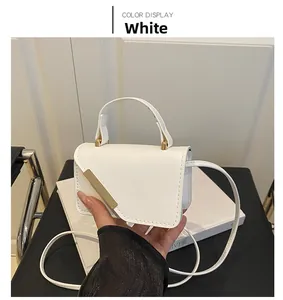 Close-up of white mini crossbody bag with gold metal trim and top handle held in hand
