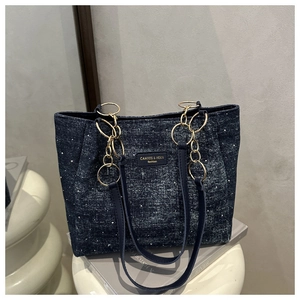 Detail of navy denim tote bag with white dot accents and gold chain straps on books