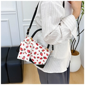 On-body shot of a white crossbody bag with red strawberry prints and black strap