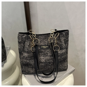 Detail of black and white tweed tote bag with gold chain strap and branding label