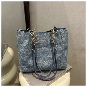 Close-up of light blue denim tote bag with white pearl accents and gold chain strap