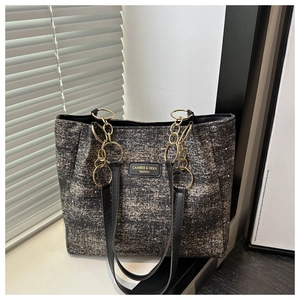 Detail of grey tweed fabric texture and black leather brand tag on a large tote bag
