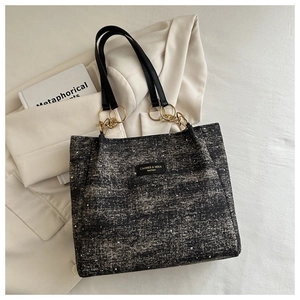 Detail of tweed tote bag with gold chain hardware and logo plate on a stylish background