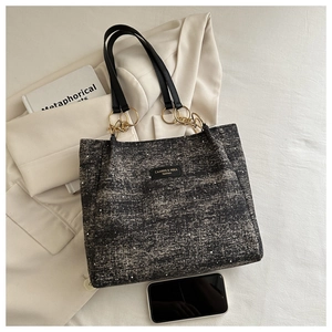 Close-up of grey tweed tote bag with gold metal chains and black leather handles