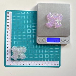 Iridescent bow-shaped collapsible phone grip stand shown with weight and size measurements