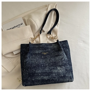 Detail of navy polka dot denim tote bag with gold chain strap and chic leather brand patch