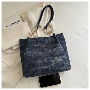 Detail of blue denim tote bag featuring golden chain straps and brand leather patch