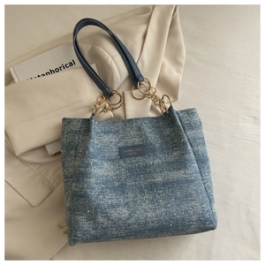 Detail of blue denim tote bag with white pearl studs and gold chain strap handle