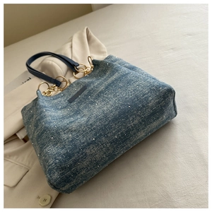 Detail of blue denim tote bag featuring silver studs and leather chain handle