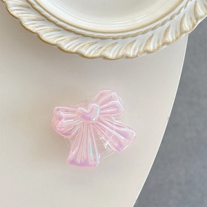 Macro view of a pink iridescent bow phone grip with heart detail on a white surface