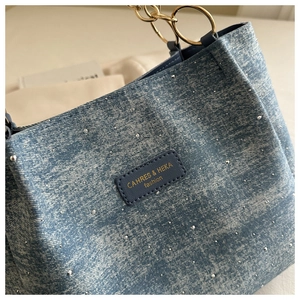Close-up of blue denim tote bag with silver studs and golden metal chain handle