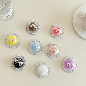 Set of 8 colorful plush bow phone grips in transparent sphere packaging on a beige desk