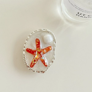 Macro detail of oval starfish phone grip with orange glitter and pearl embellishment