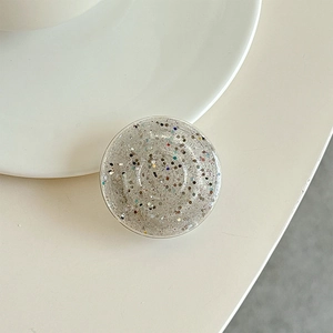 Close-up of a round silver glitter phone grip with colorful sequins on a white desk