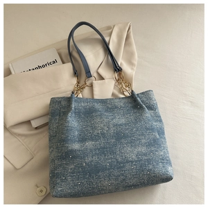 Detail of blue denim tote bag with gold chain straps and shimmering rhinestone accents