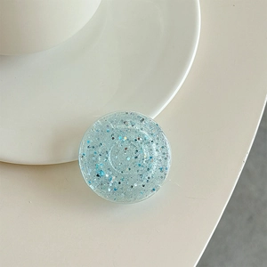 Close-up of a round blue glitter phone grip with silver sequins on a minimalist surface