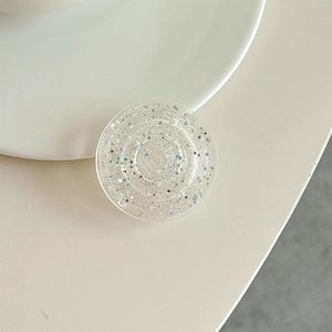 Detail of round glitter phone grip with silver sequins on a cream-colored desk