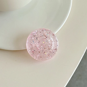 Close-up of pink glitter folding phone socket grip on a minimalist beige desk setup