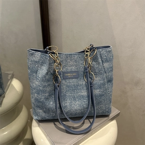 Blue denim tote bag with pearl accents and gold chain strap on a minimalist display