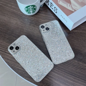 Close-up of silver glitter phone cases for iPhone on a wooden desk with lifestyle props