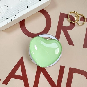 Close-up of heart-shaped glass phone grip with reflective green finish on a lifestyle tray