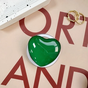 Detail of a shiny green heart-shaped phone grip on a stylish background with gold rings