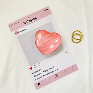 Dettaglio del supporto per telefono a cuore rosa lucido con eleganti anelli in metallo oro