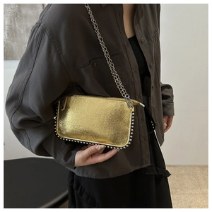 Close-up of golden metallic chain bag with silver studs and chain strap on a model