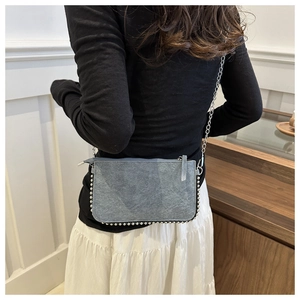 Detail of blue denim texture crossbody bag with silver studs and metal chain strap