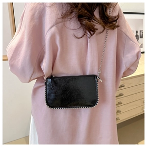 Detail of a black glossy leather crossbody bag with silver beaded rivets and metal chain