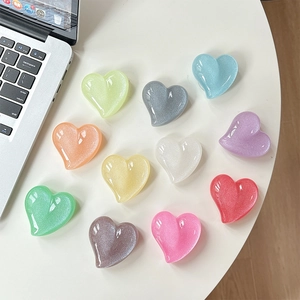Glittery heart-shaped phone grip sockets in pastel colors arranged on a white desk