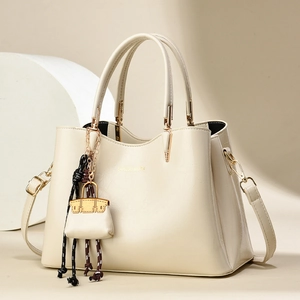 Sac à main crème élégant avec poignées rondes et pendentif miniature en studio
