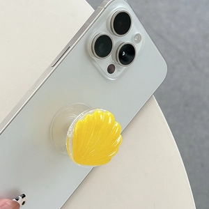 Detailed view of yellow glitter shell-shaped phone grip on white smartphone case