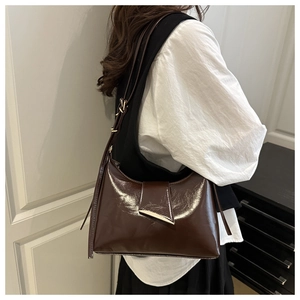 Detail of dark brown patent leather shoulder bag with a metallic triangle buckle on model