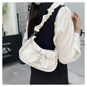 Detail of creamy baguette bag featuring ruffled shoulder strap and pearl floral chain