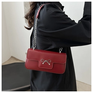 Detail of dark red matte leather shoulder bag featuring silver metal bow and chain strap