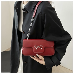 Détail d'un sac rouge avec une boucle en nœud argenté et une bandoulière chaîne
