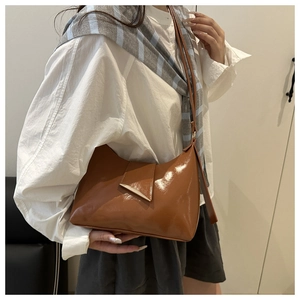 Detail of caramel brown underarm bag showing the sleek leather and gold triangle buckle