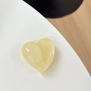 Macro shot of a light yellow heart-shaped phone grip with glitter finish on a white surface