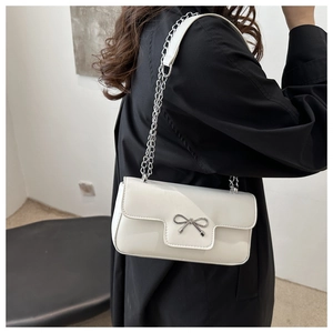 Detail of cream white faux leather shoulder bag with silver bow and metal chain strap