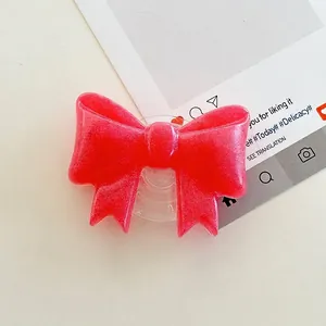 Close-up of a red glitter bow-shaped folding phone grip on a minimalist desk