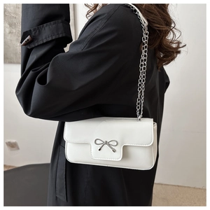 Detail of white glossy shoulder bag featuring silver metal bow and fine chain strap