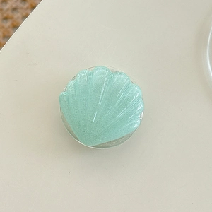 Macro view of shell-shaped pale green glitter phone grip with pearlescent finish