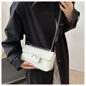 Détail d'un sac à bandoulière en cuir blanc avec nœud argenté et chaîne sur manteau noir