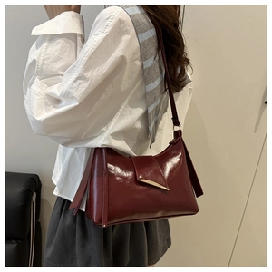 Detail of burgundy glossy leather shoulder bag with gold spiked hardware on model