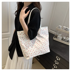Close-up of white tote bag with red cherry prints and white shoulder strap on a model