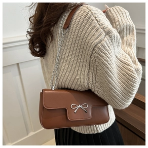 Sac bandoulière marron en similicuir avec nœud argenté porté sur un pull en maille beige