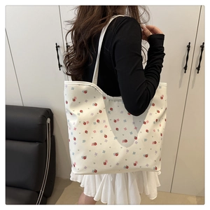 Close-up of strawberry and floral print tote bag worn on shoulder in minimalist interior