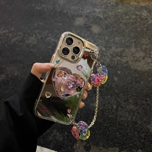 Macro detail of mirrored iPhone case featuring a 3D crystal heart and colorful beaded strap